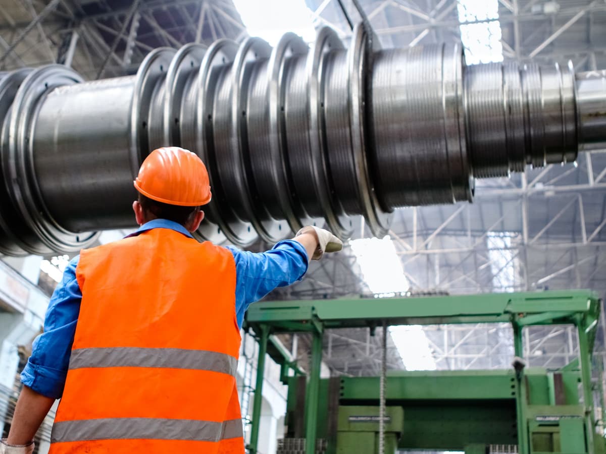 Técnico de colete refletivo e capacete inspecionando equipamento de grande porte dentro de uma planta industrial